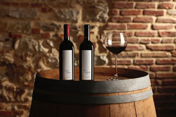 Bottiglie di Tenuta Bettina e Rosso del Gallo accanto a un calice di vino rosso su una botte in cantina